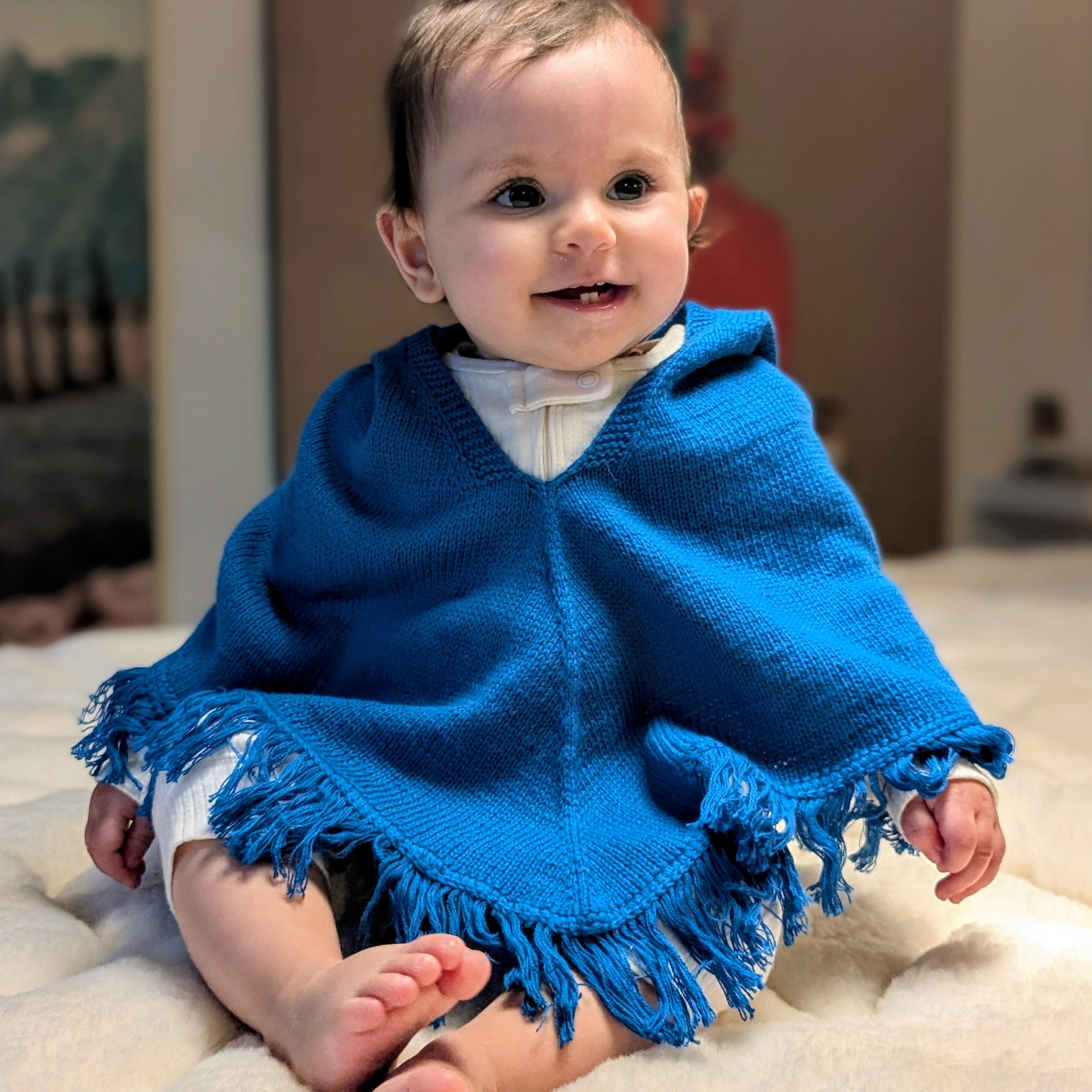 Baby wearing a blue poncho sitting on a light-colored surface.