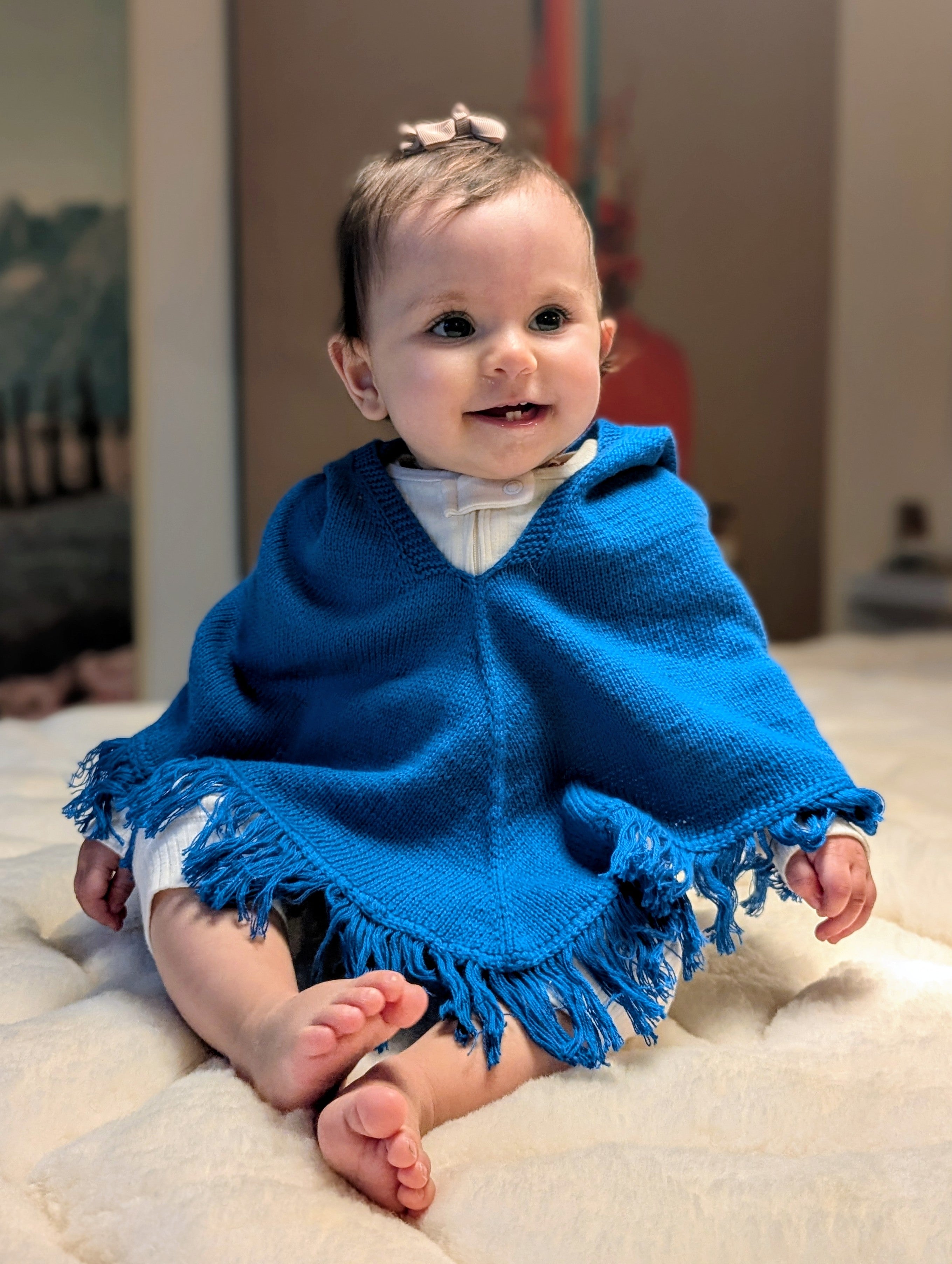 Baby wearing a blue poncho sitting on a light-colored surface.