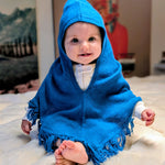 Baby wearing a blue hooded poncho sitting on a white surface.