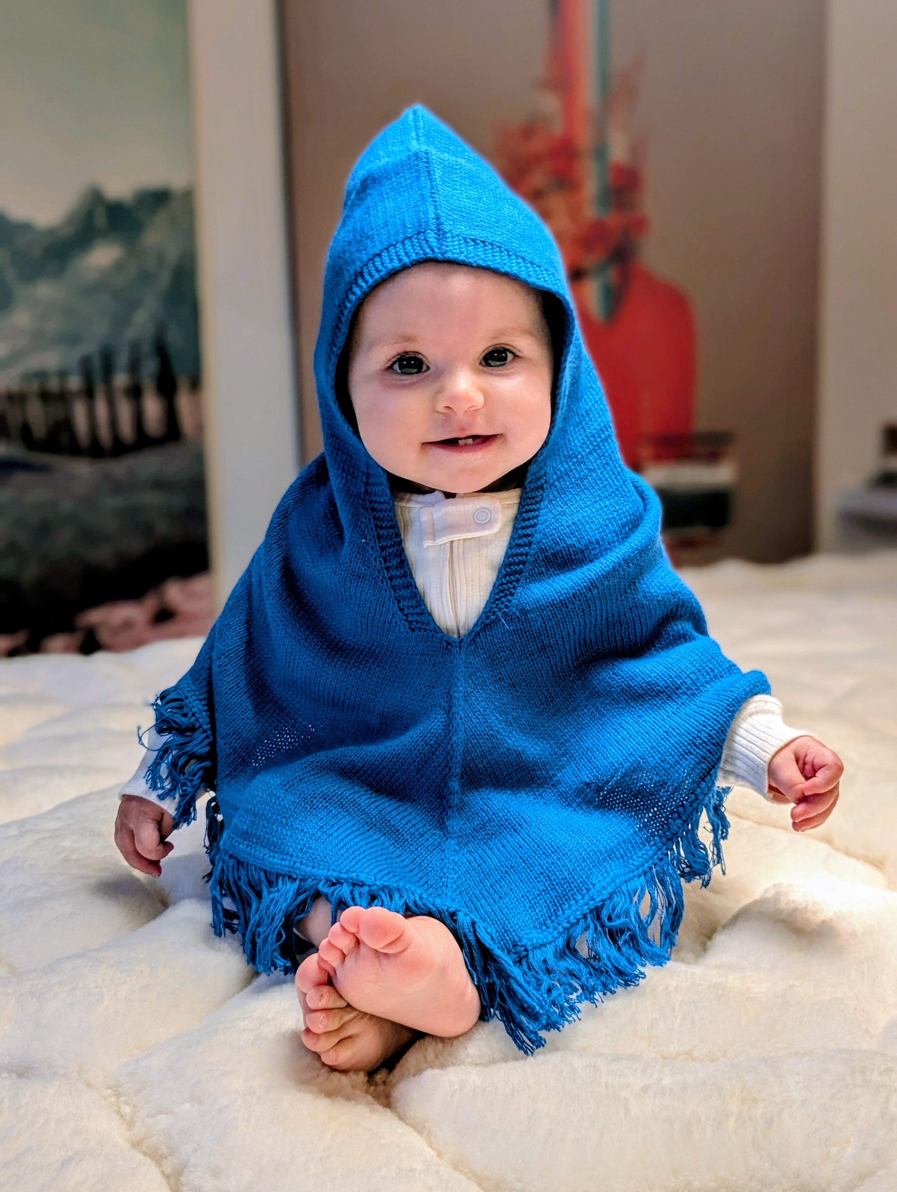 Baby wearing a blue hooded poncho sitting on a white surface.