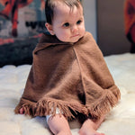 Baby wrapped in a brown blanket sitting on a white surface with colorful background