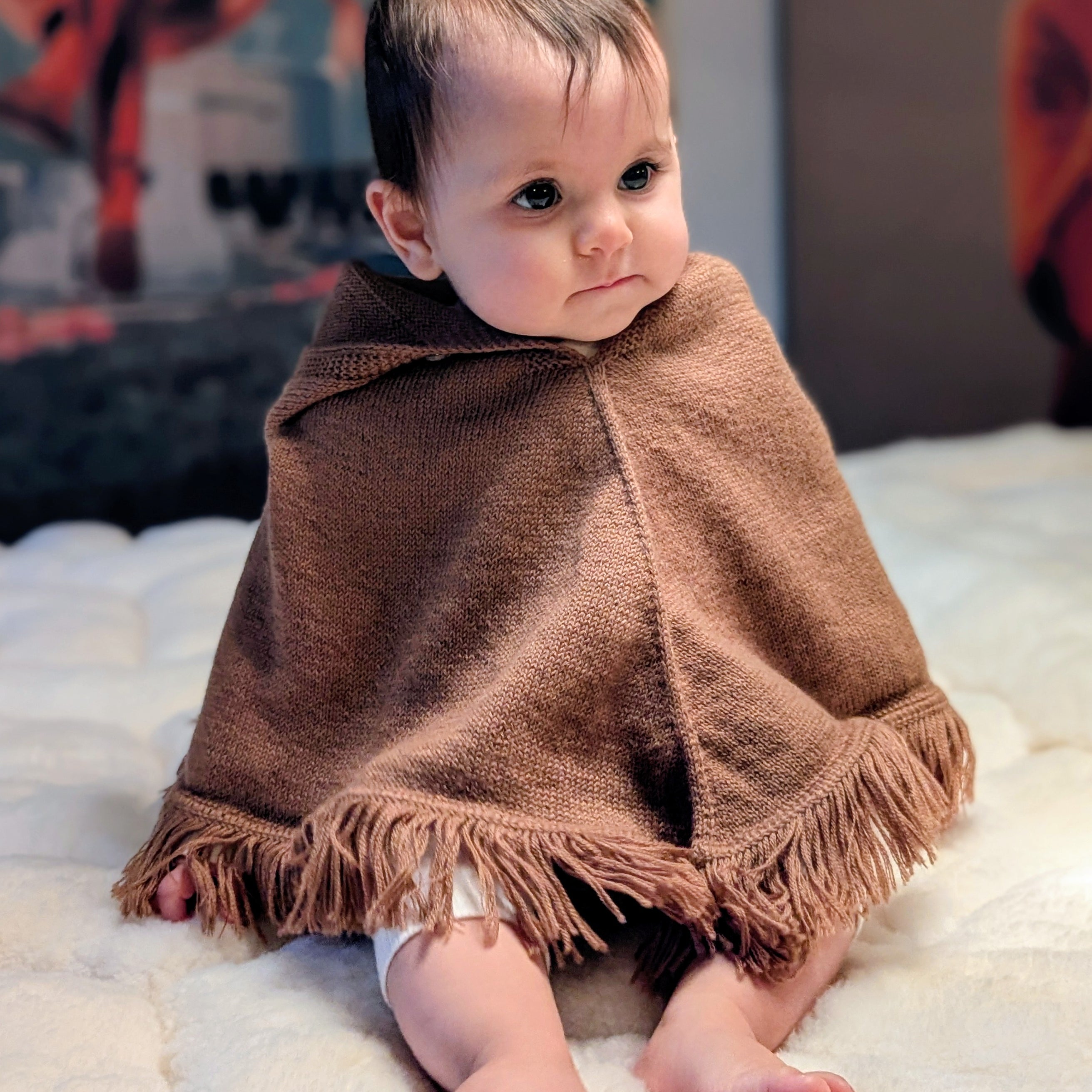 Baby wrapped in a brown blanket sitting on a white surface with colorful background