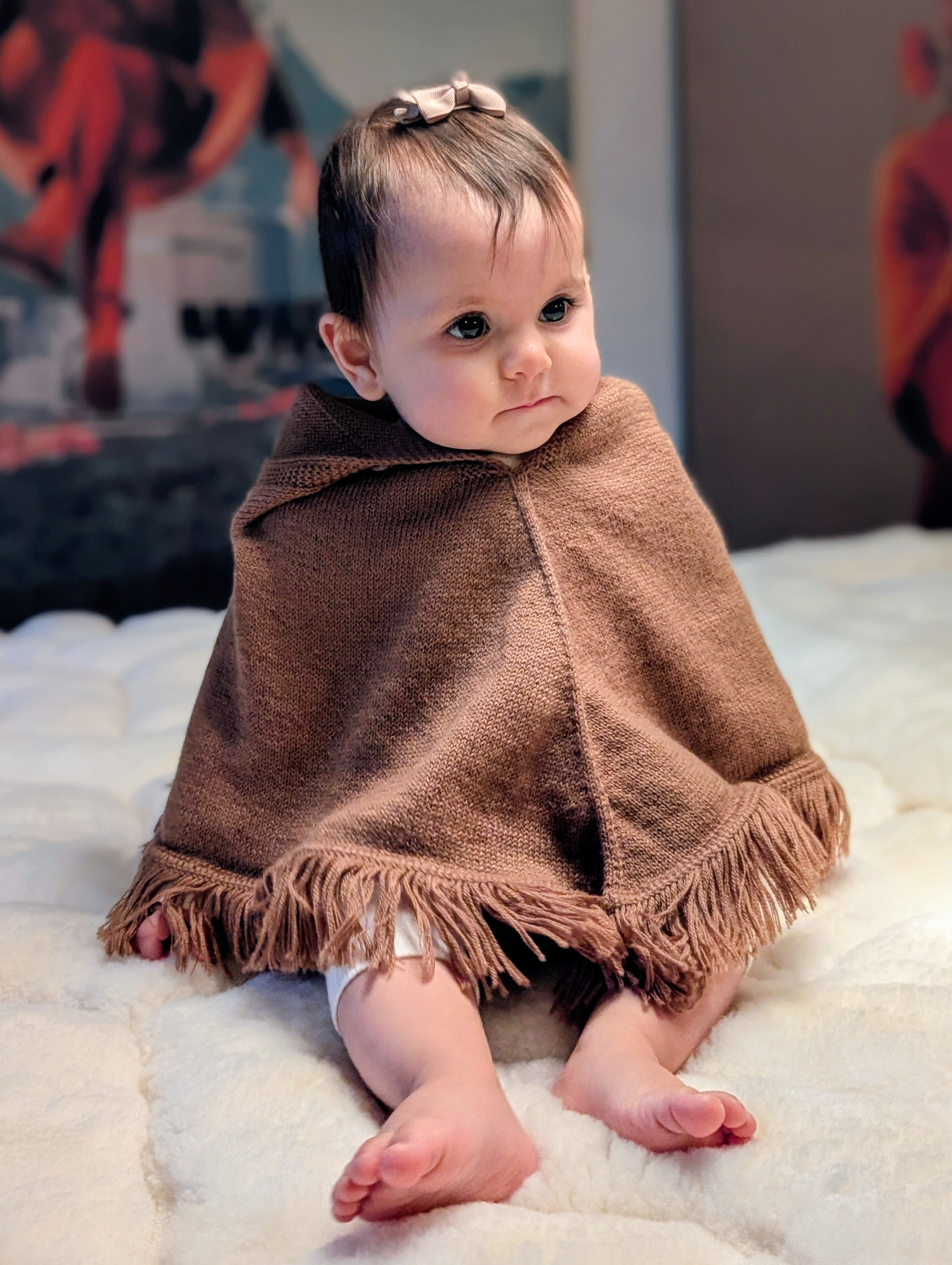 Baby wrapped in a brown blanket sitting on a white surface with colorful background