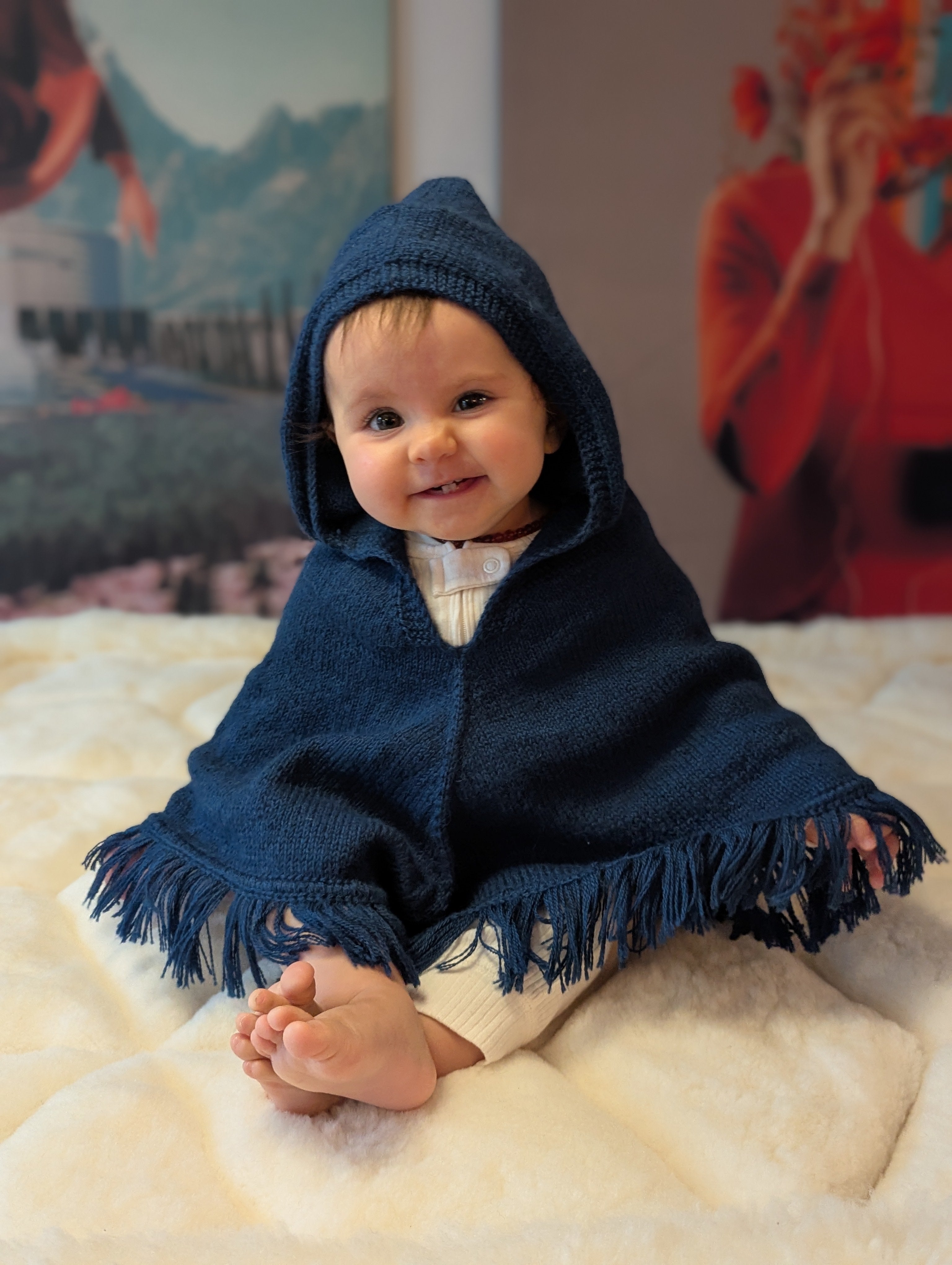 Baby wearing a blue hooded poncho sitting on a white surface with colorful abstract art in the background.