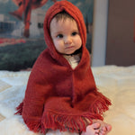 Baby wrapped in a red hooded blanket on a soft surface with a blurred background