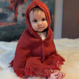 Baby wrapped in a red hooded blanket on a soft surface with a blurred background
