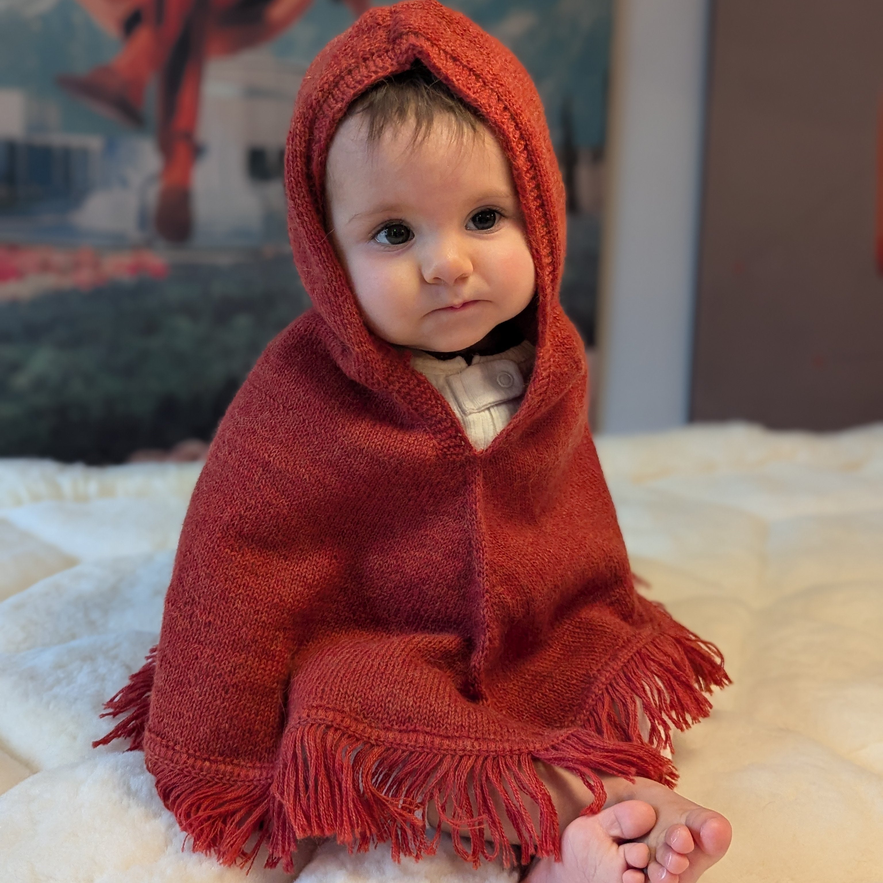 Baby wrapped in a red hooded blanket on a soft surface with a blurred background
