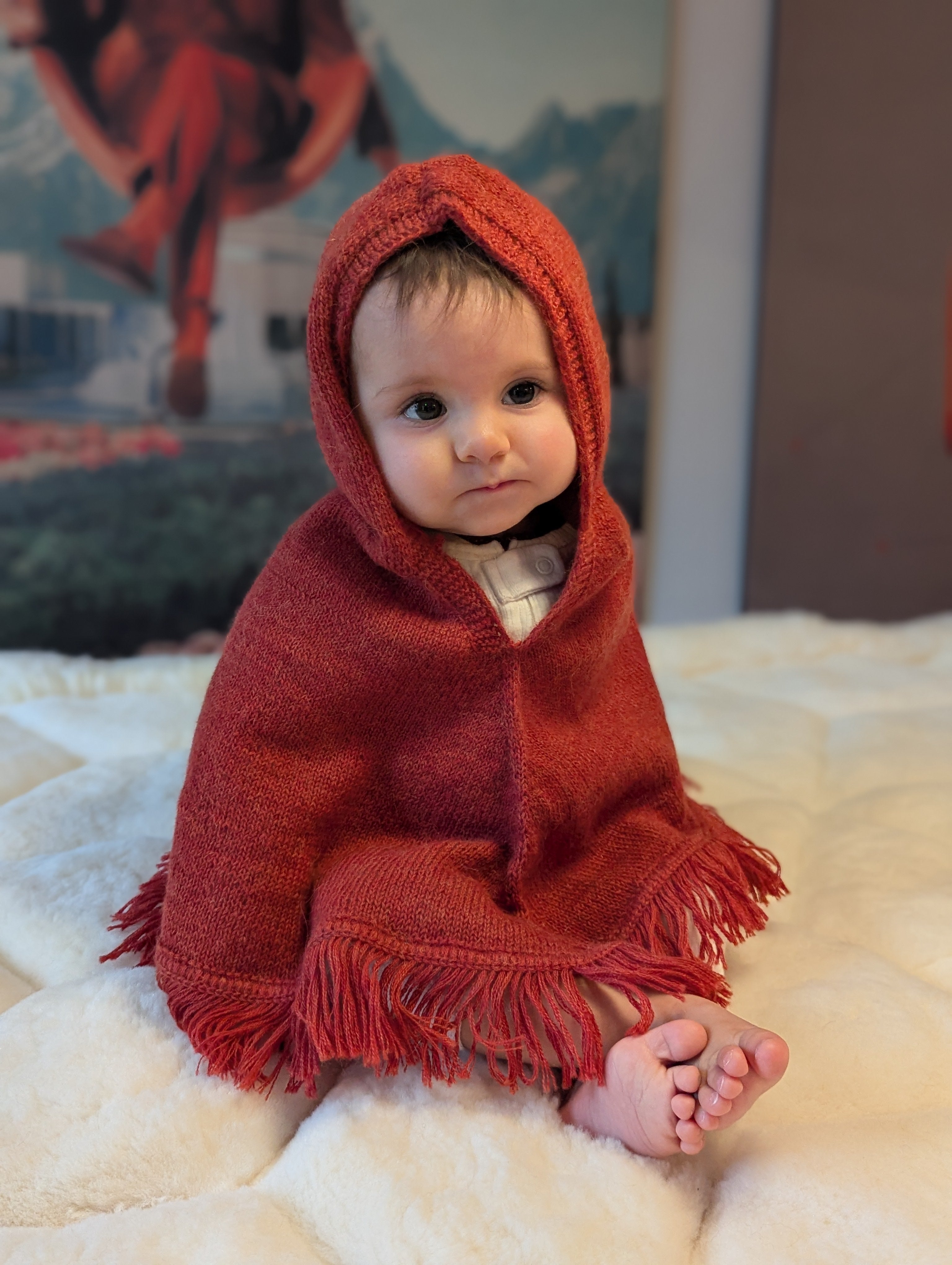 Baby wrapped in a red hooded blanket on a soft surface with a blurred background