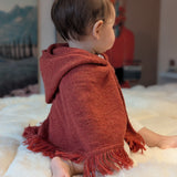Child wearing a red hooded poncho sitting on a white surface with a blurred background