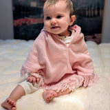 Baby wearing a pink blanket sitting on a white surface with a blurred background