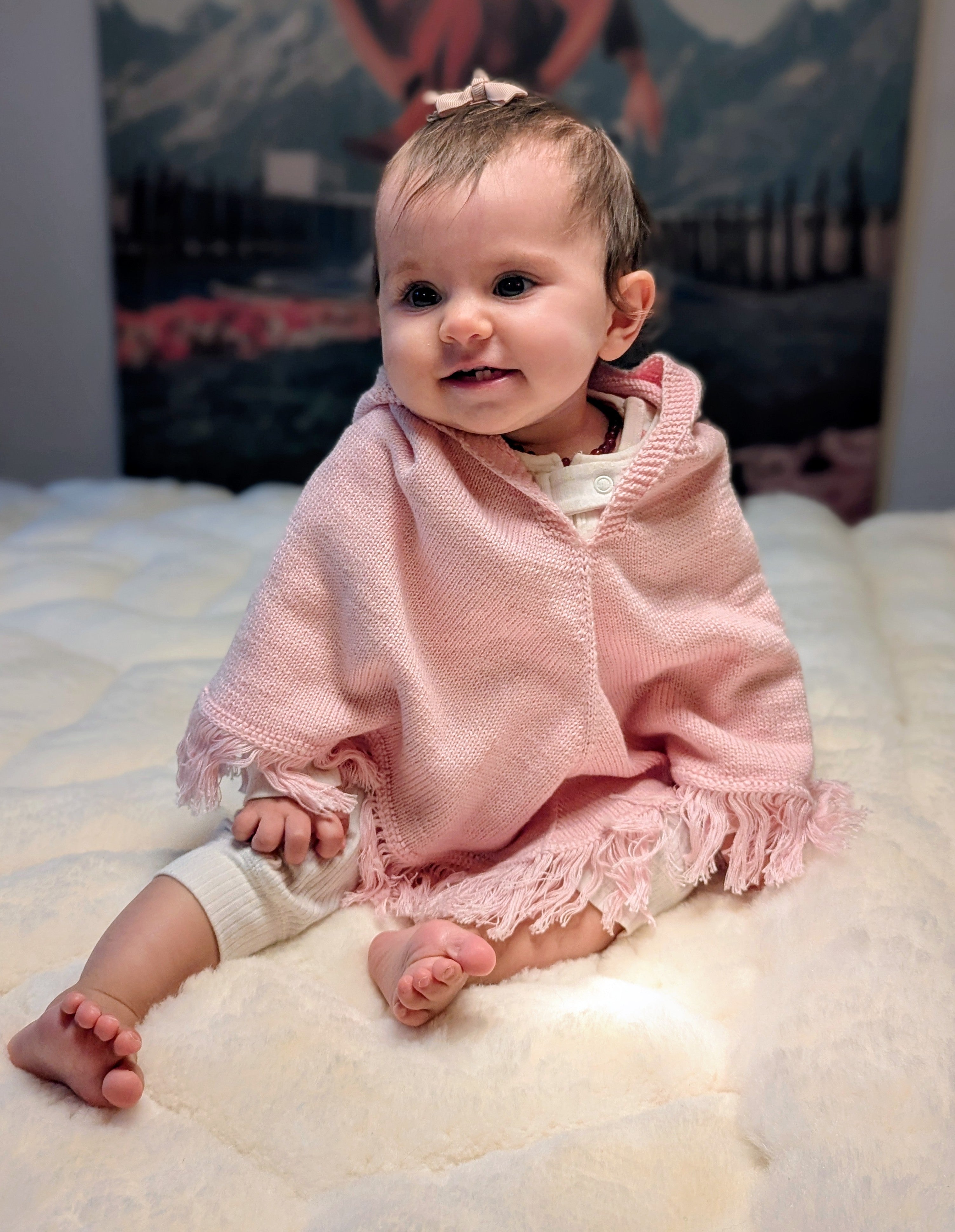 Baby wearing a pink blanket sitting on a white surface with a blurred background