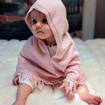 Baby wearing a pink knitted hooded garment on a white surface