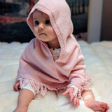 Baby wearing a pink knitted hooded garment on a white surface