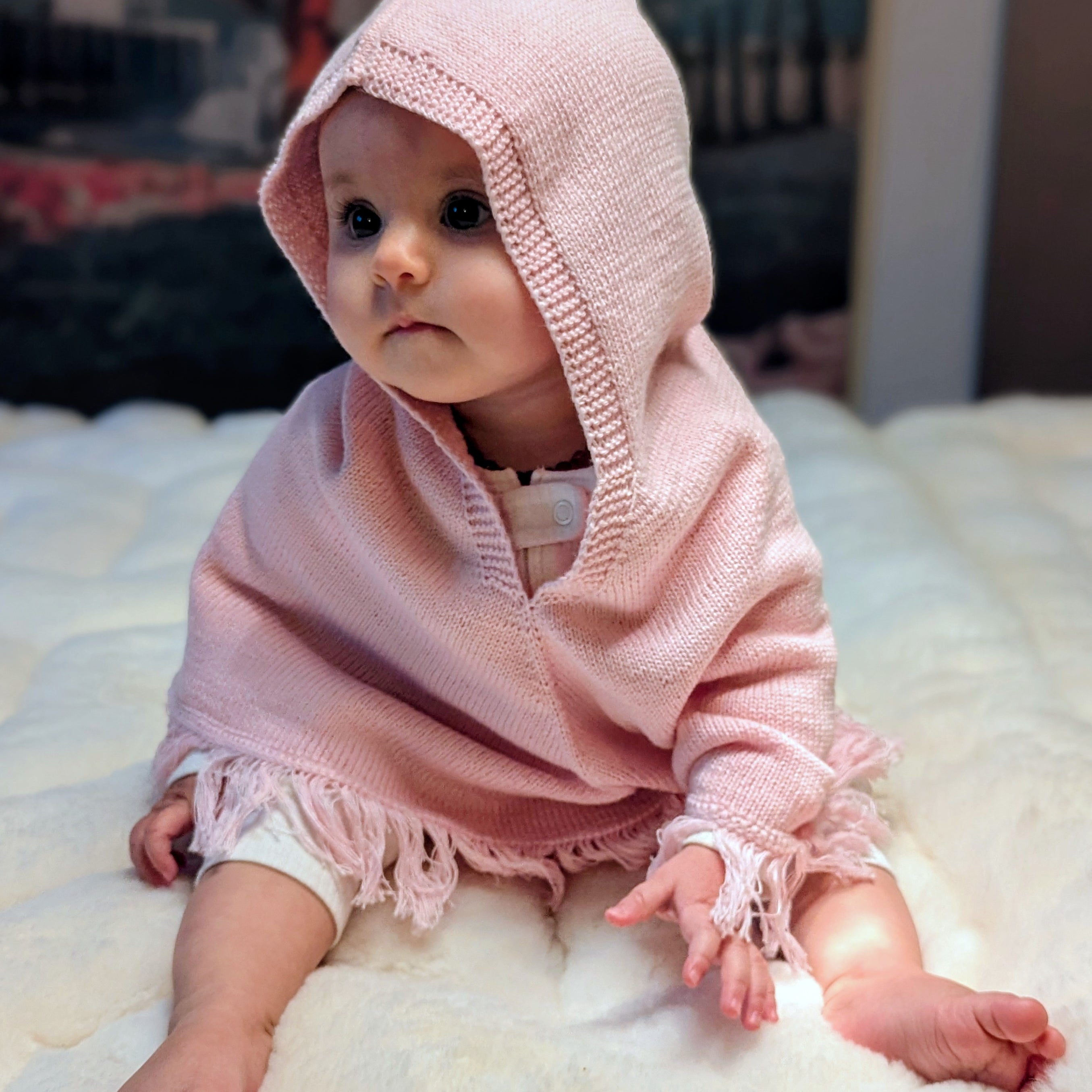 Baby wearing a pink knitted hooded garment on a white surface