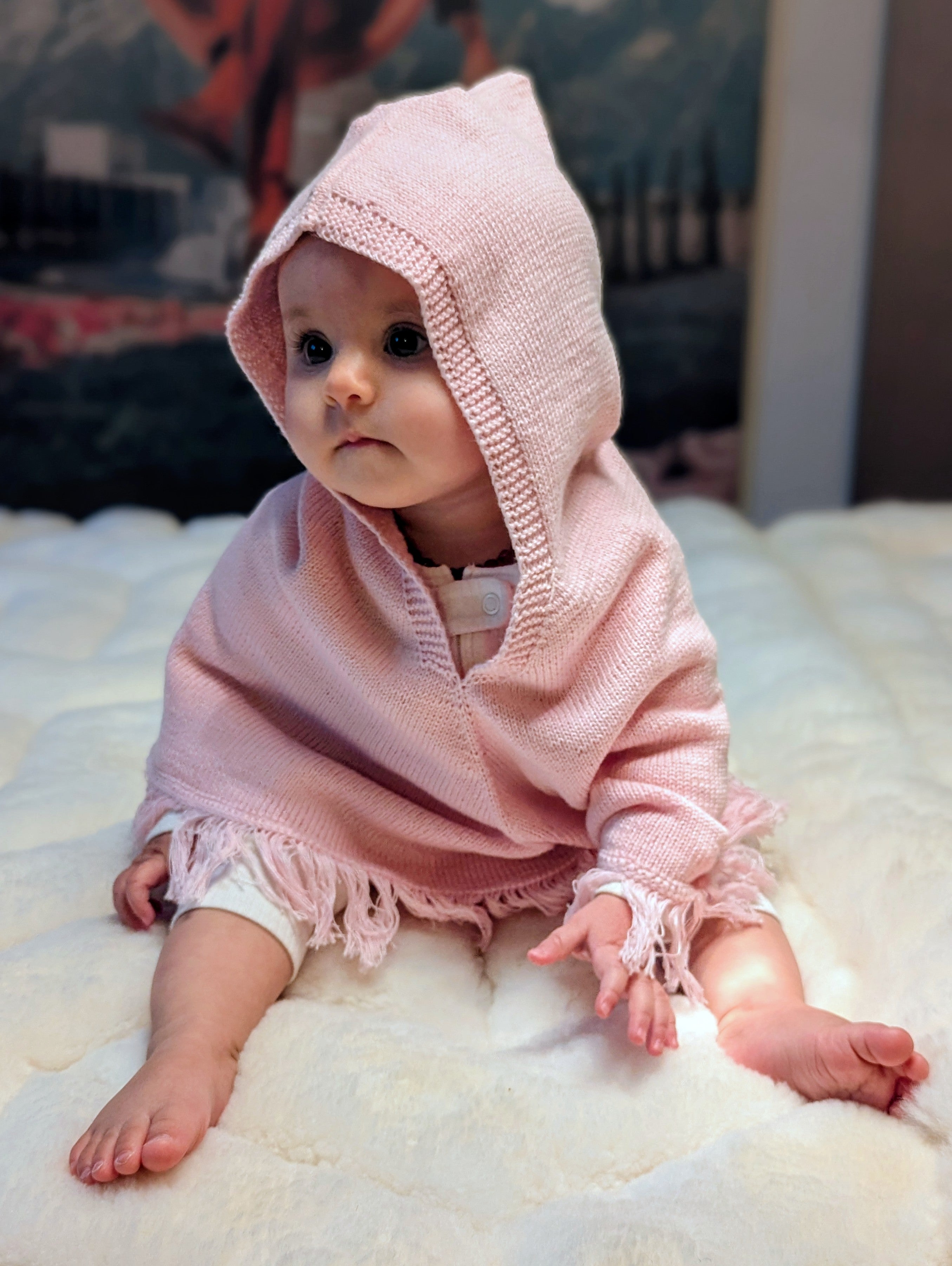 Baby wearing a pink knitted hooded garment on a white surface