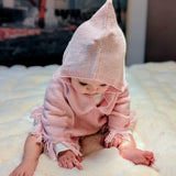 Baby wearing a pink knitted outfit with a hood on a white blanket.