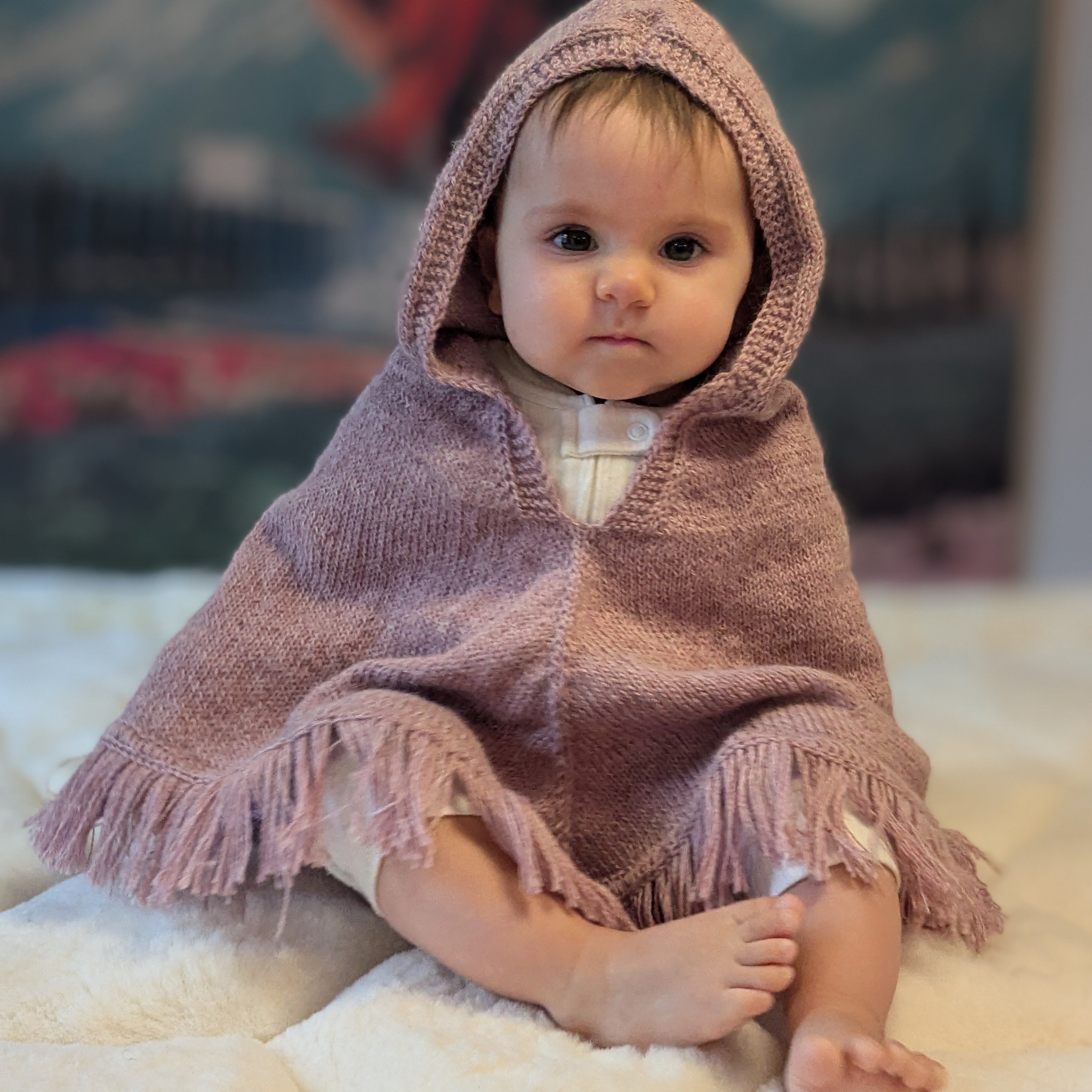 Baby in a pink hooded blanket sitting on a soft surface with a blurred background