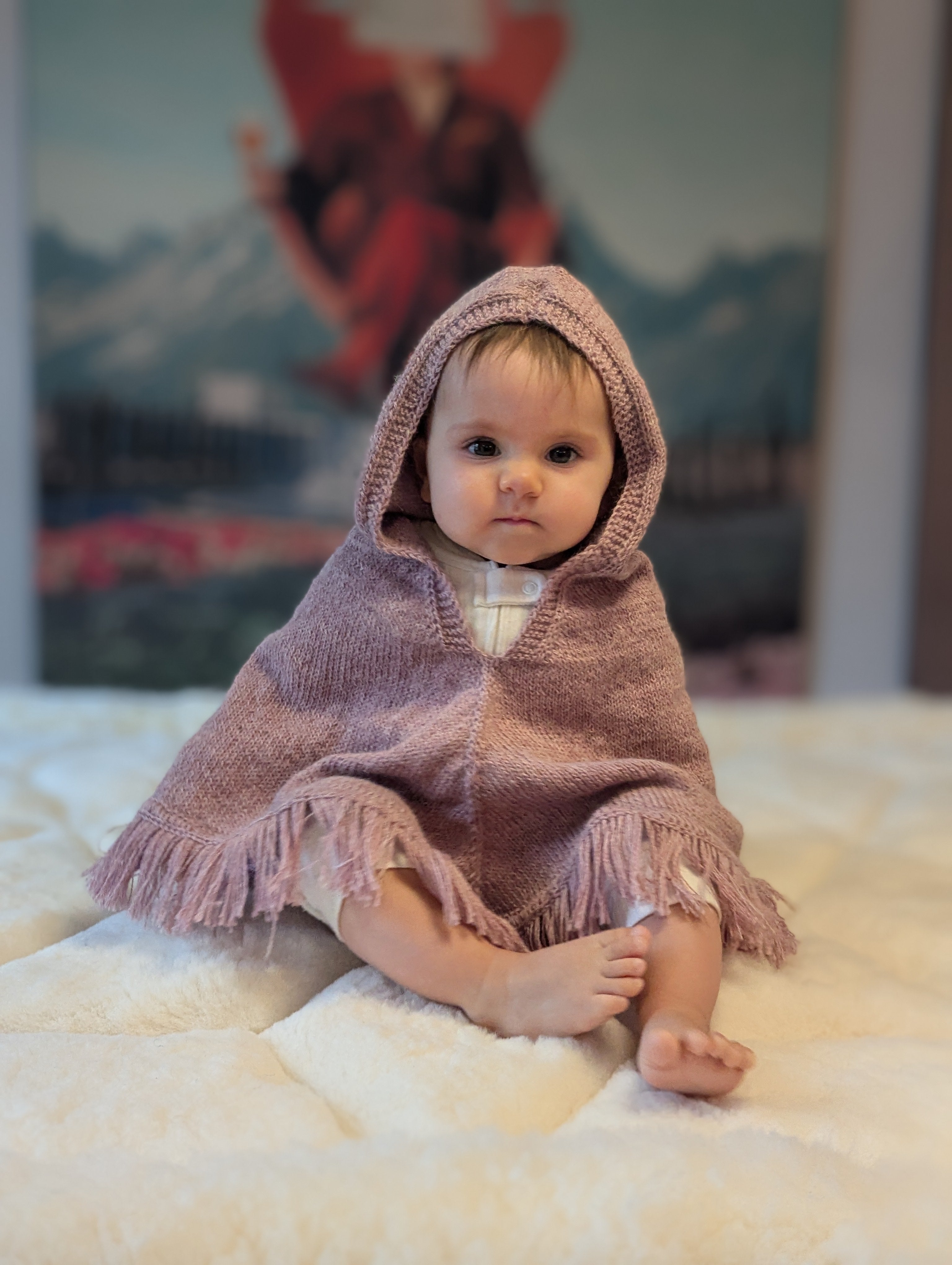 Baby in a pink hooded blanket sitting on a soft surface with a blurred background
