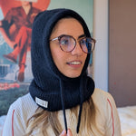 Woman wearing a black knitted balaclava with a logo, indoors.