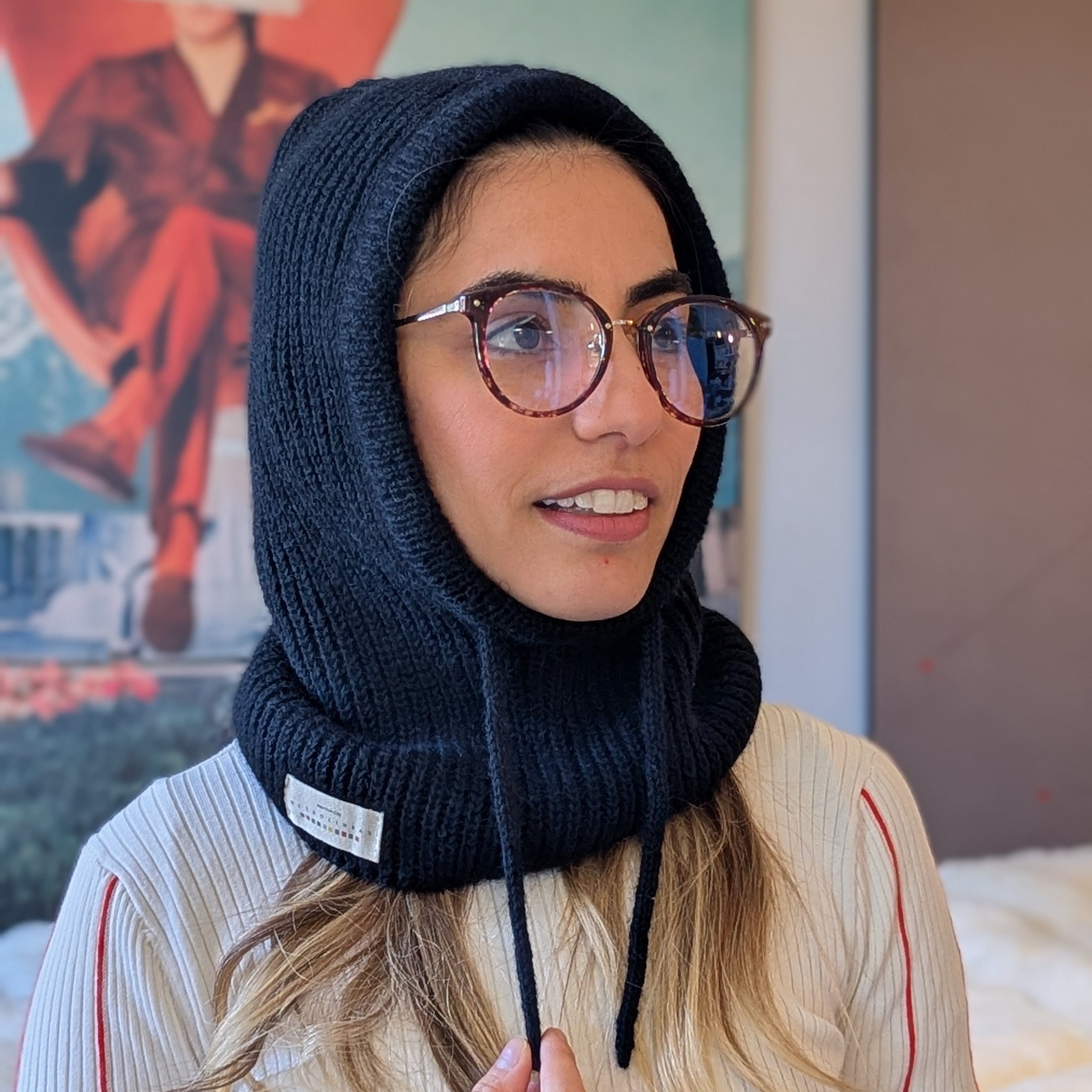 Woman wearing a black knitted balaclava with a logo, indoors.