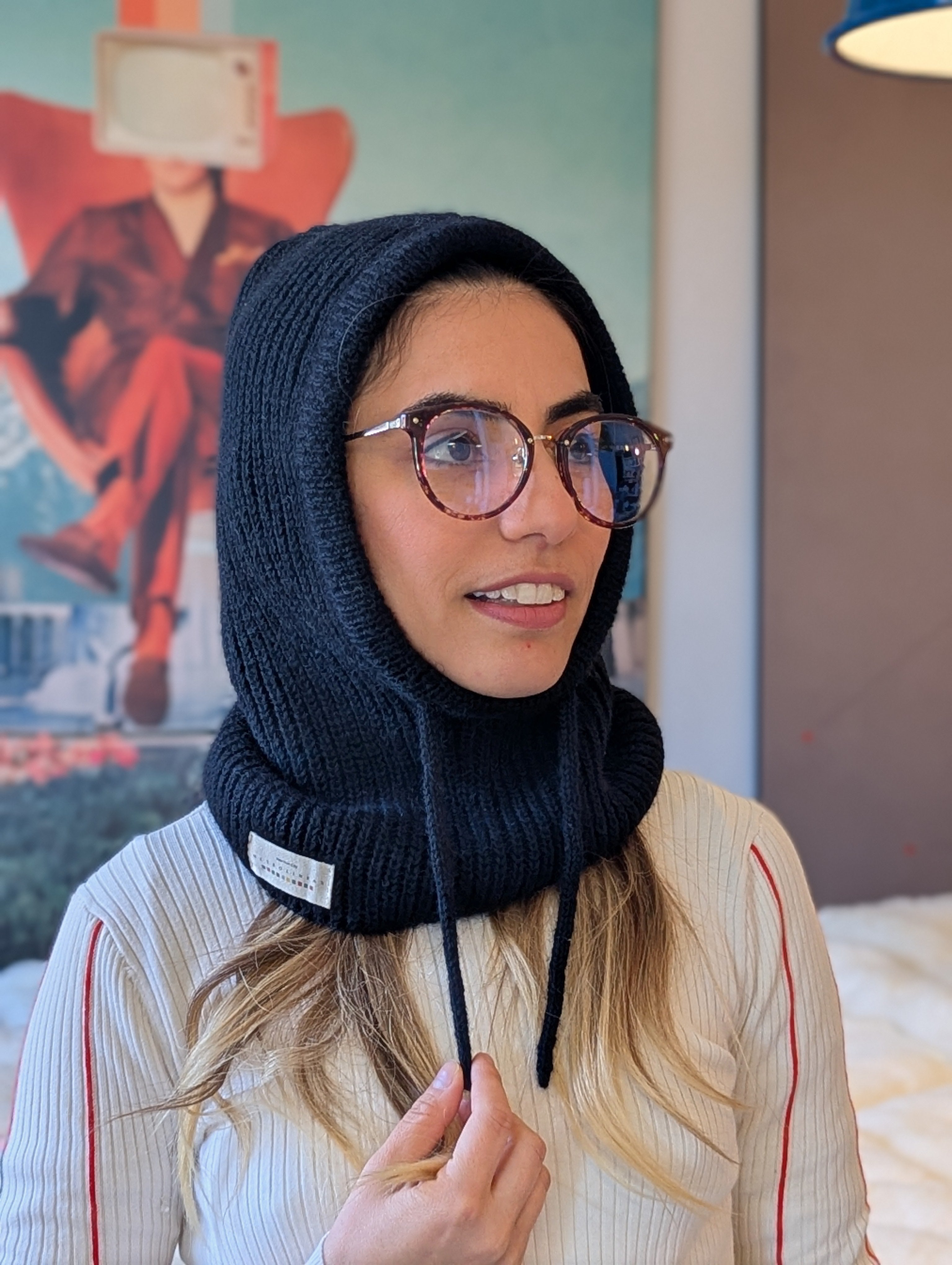 Woman wearing a black knitted balaclava with a logo, indoors.