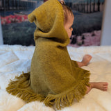Child wearing a mustard knitted poncho with fringe on a white blanket