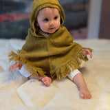 Baby wearing a mustard hooded poncho sitting on a white surface with a blurred background