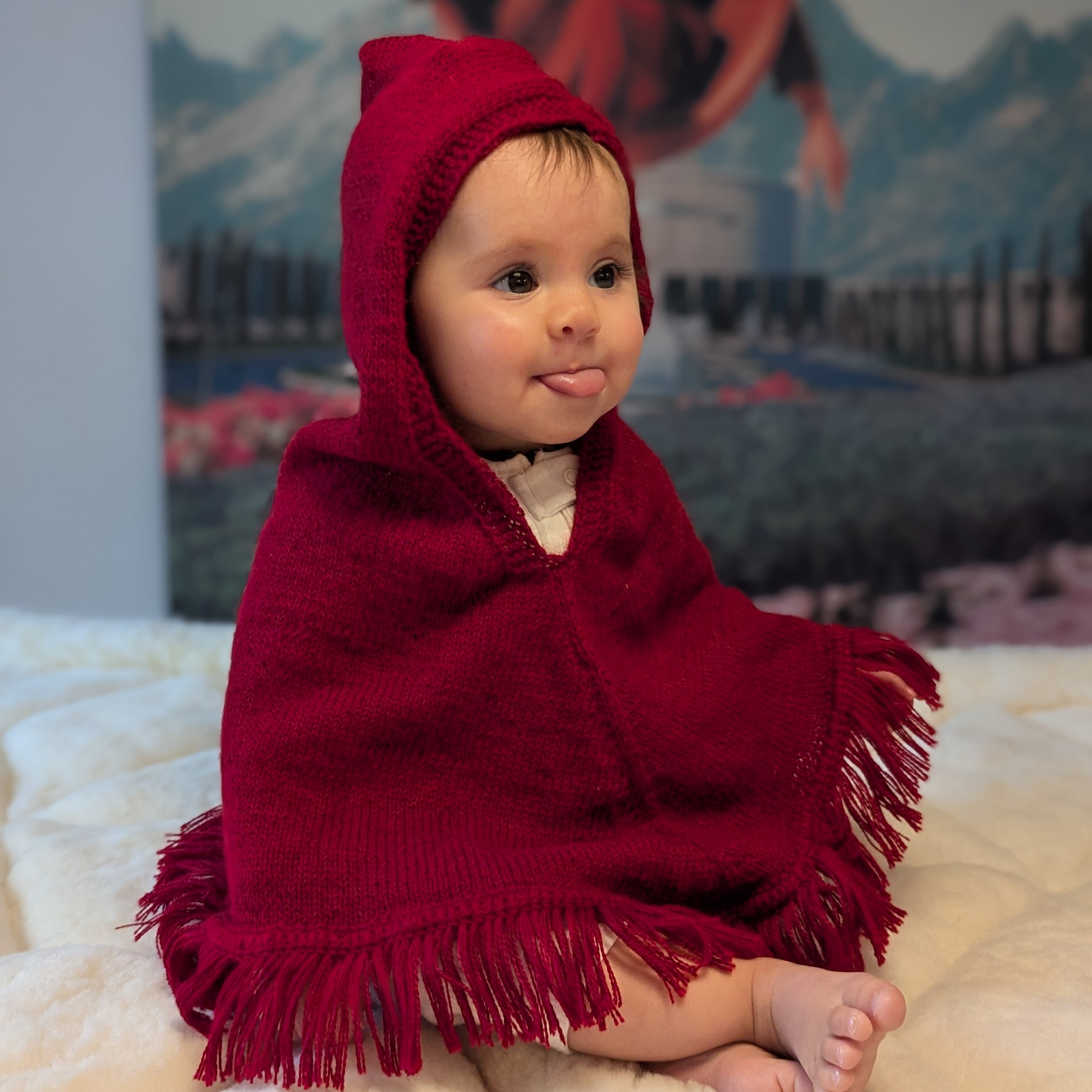 Baby wrapped in a red hooded blanket sitting on a white surface with a blurred background