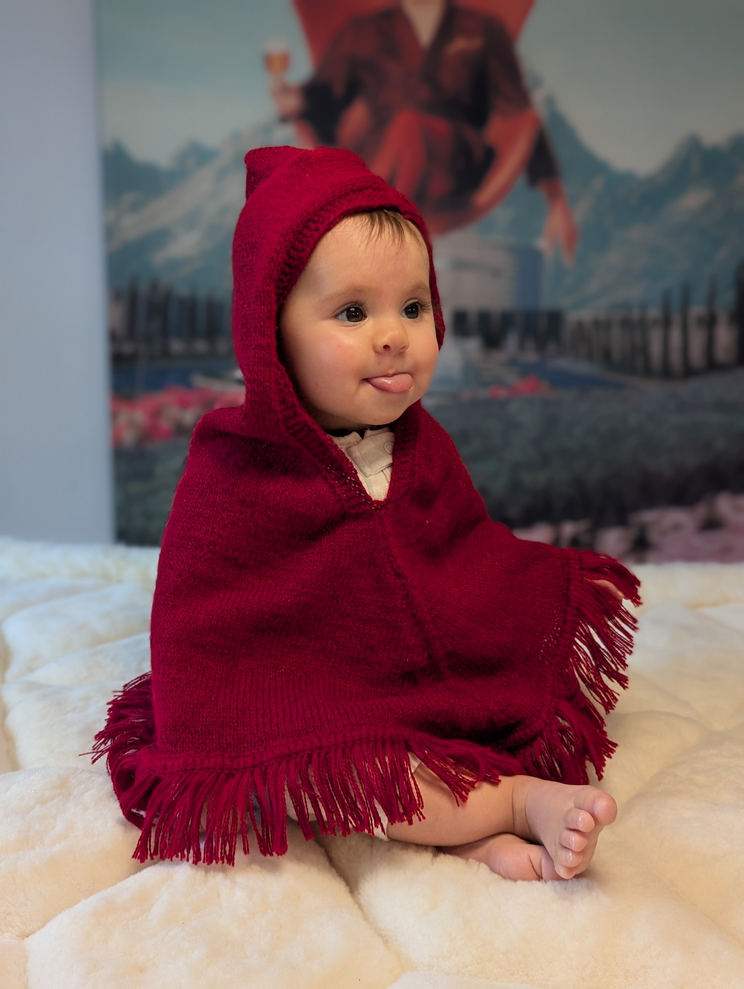 Baby wrapped in a red hooded blanket sitting on a white surface with a blurred background