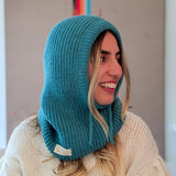 Person wearing a teal knitted hood over a white sweater