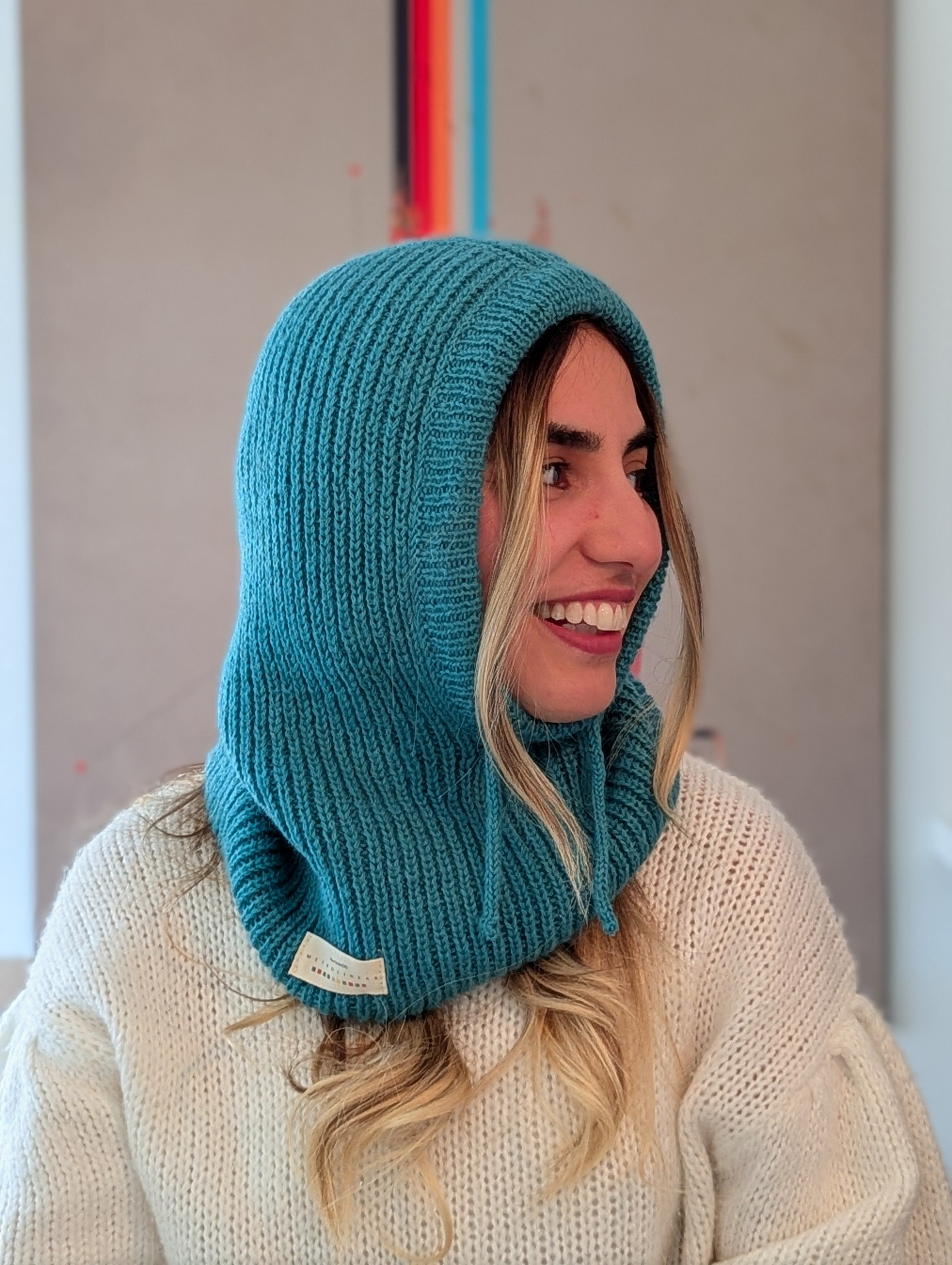 Person wearing a teal knitted hood over a white sweater