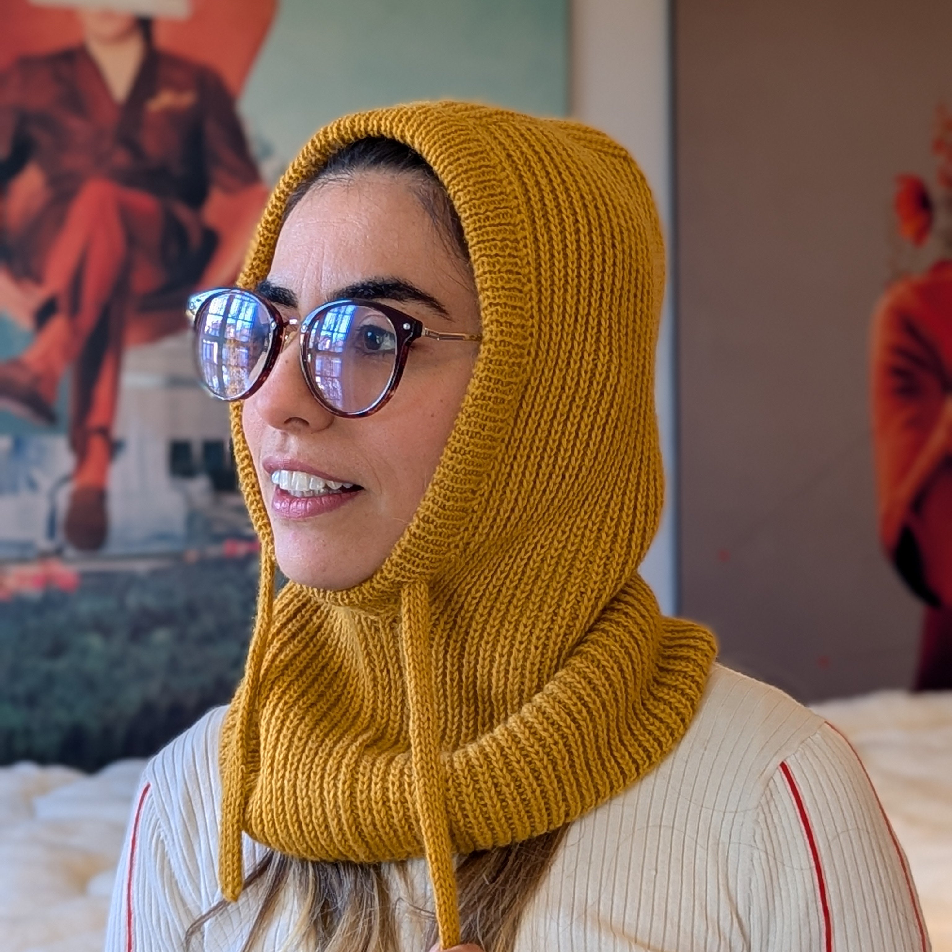 Woman wearing a mustard yellow knitted hood in an indoor setting
